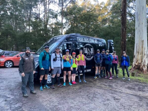 the group runners stand in a line in front of the trail bus at the campsite before starting the trail run