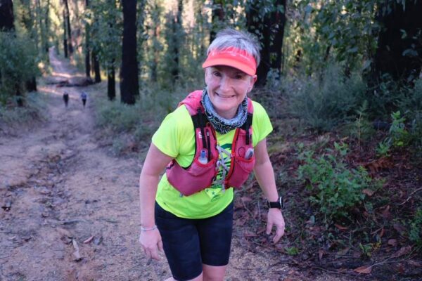 a smiling female runner as she hikes up a hill surrounded by forest